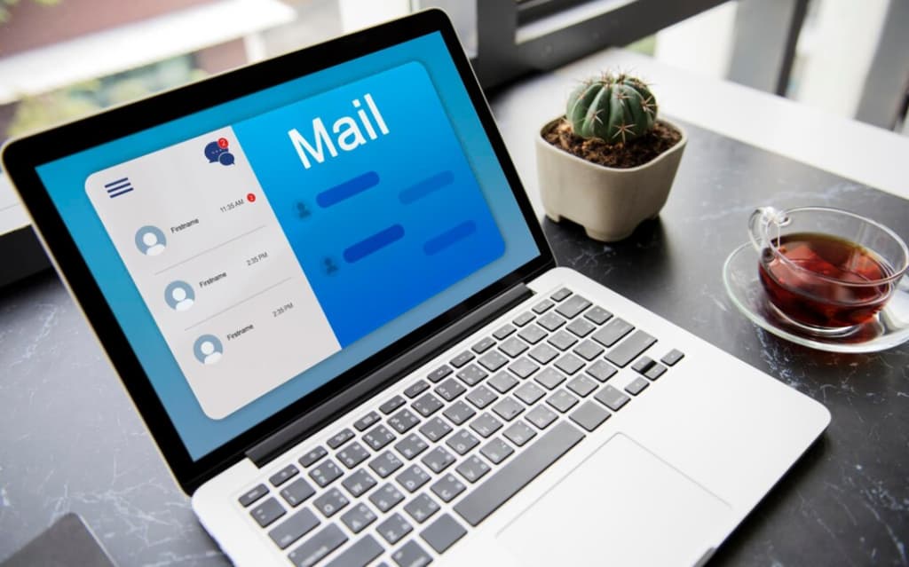 A laptop with an email interface onscreen beside a cup of tea and a cactus